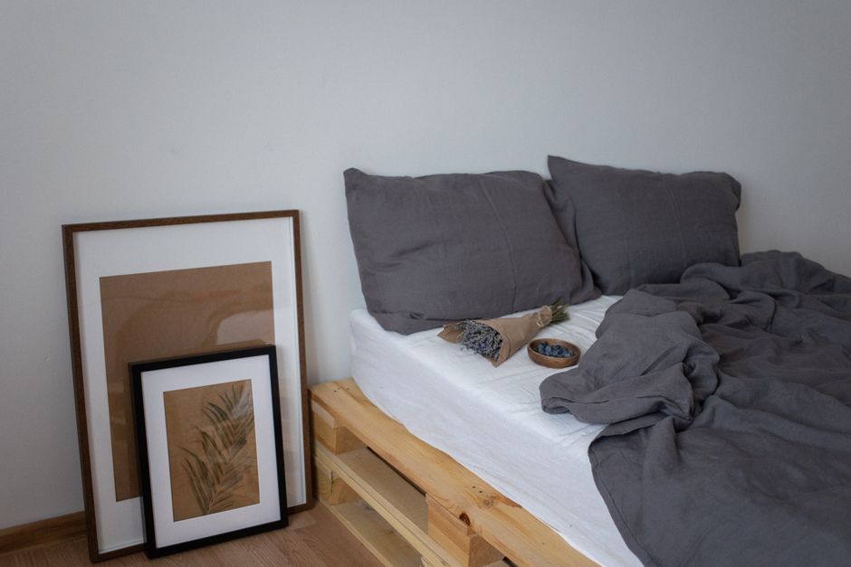 Stylish minimalist bedroom featuring grey bedding and framed art on wooden pallet bed.